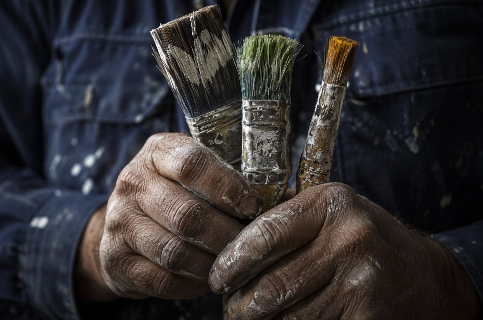 Manos de pintor profesional sosteniendo brochas usadas con restos de pintura